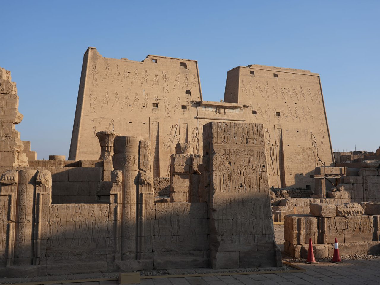 The grand first pylon of the Temple of Edfu framed by ancient stone ruins
