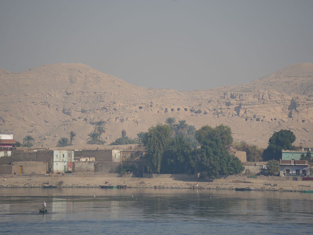 Ancient rock-cut tombs overlooking a peaceful village along the Nile River
