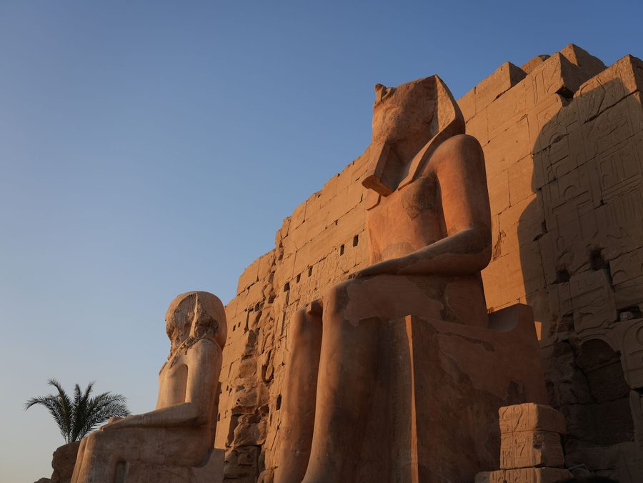 The colossal seated statues of Ramesses II illuminated by sunset in front of the pylon at Karnak Temple