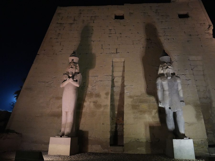 The illuminated colossal statues of Ramesses II in front of the pylon at Luxor Temple at night