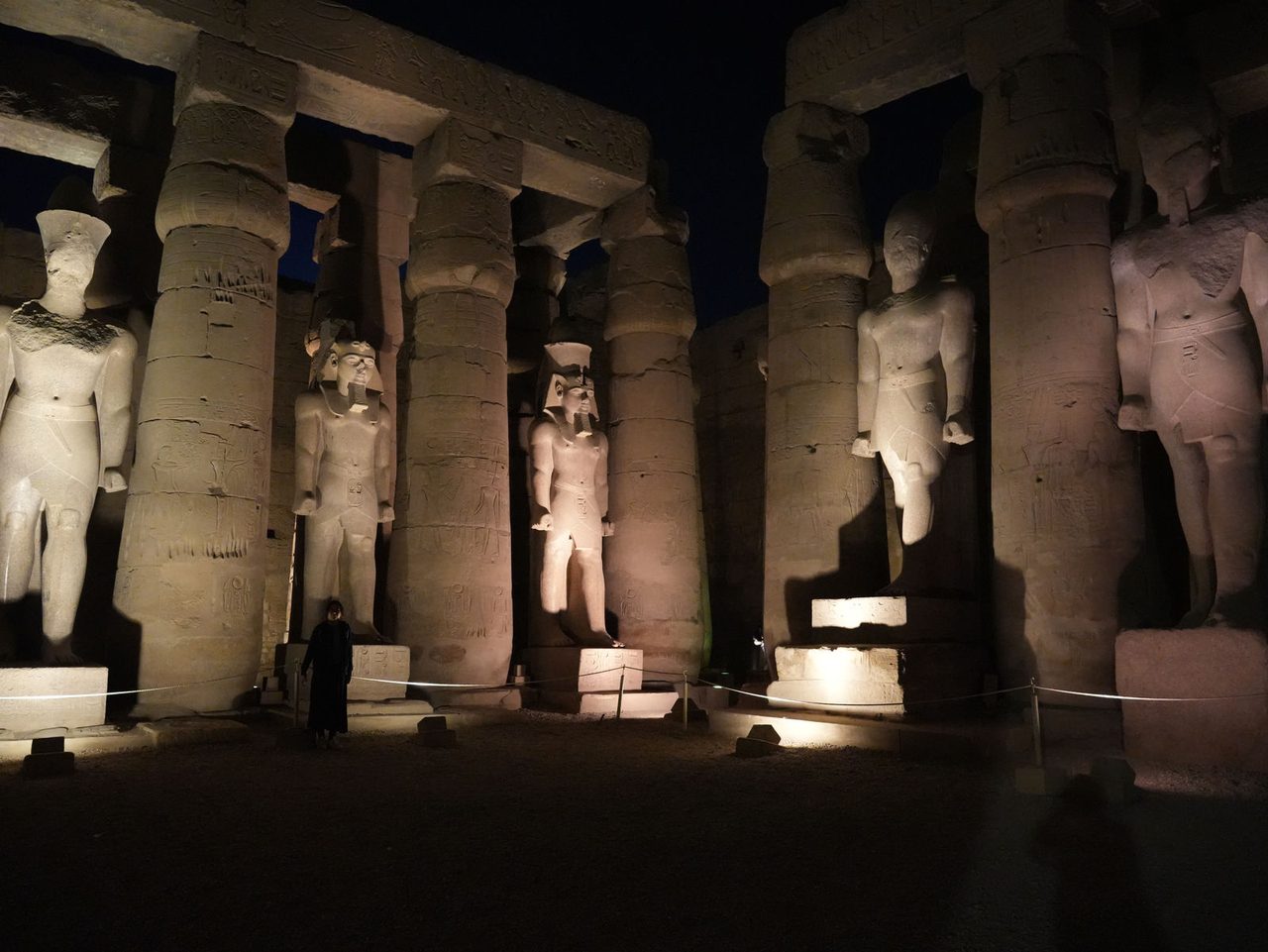 The illuminated colossal statues of Ramesses II standing between the columns in the peristyle court of Luxor Temple at night