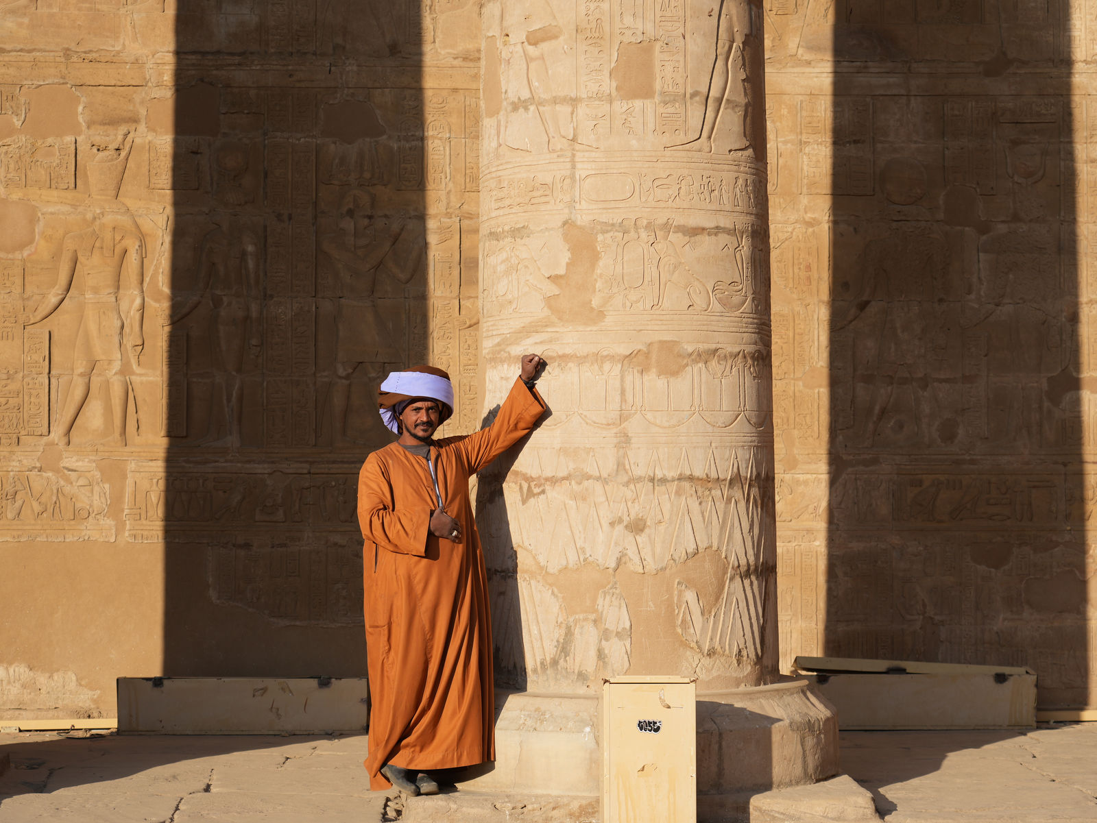 A local guardian in traditional galabeya leaning against the ancient columns of Edfu