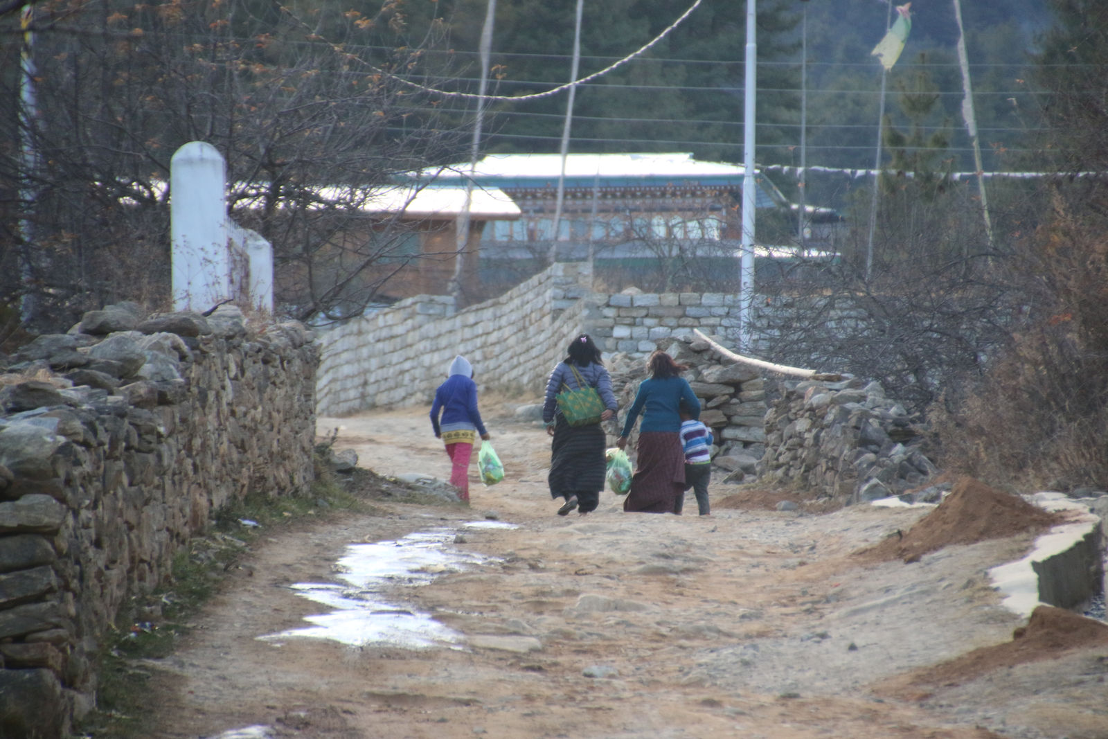 Local villagers walking along a rustic dirt road lined with stone walls